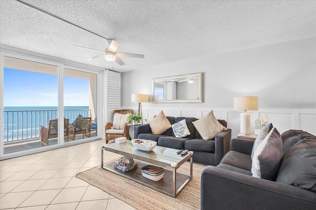 living room featuring ceiling fan, light tile patterned floors, a water view, and a textured ceiling