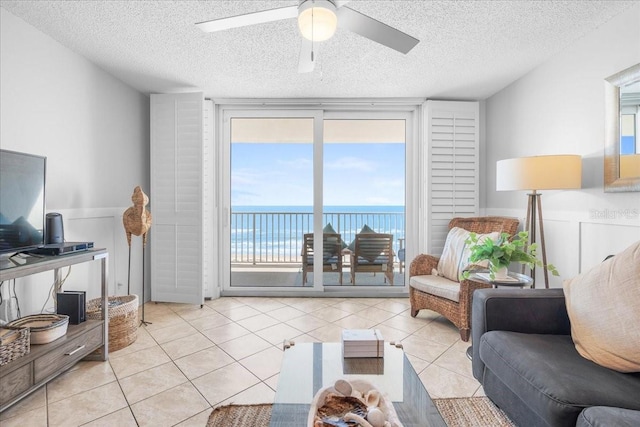 tiled living room featuring ceiling fan, a water view, and a textured ceiling