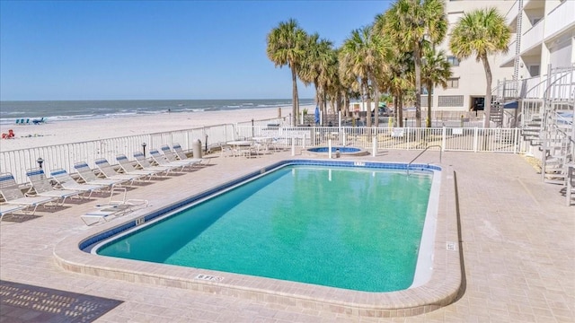 view of swimming pool featuring a patio area, a water view, and a beach view