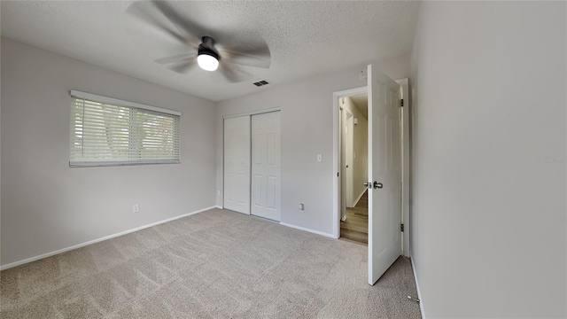 unfurnished bedroom with ceiling fan, a closet, light carpet, and a textured ceiling