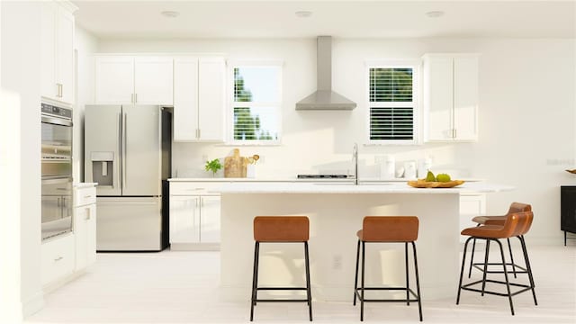 kitchen featuring white cabinets, a kitchen breakfast bar, wall chimney range hood, appliances with stainless steel finishes, and a kitchen island