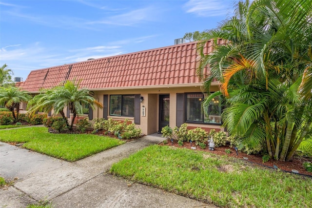 view of front facade featuring a tile roof, a front yard, and stucco siding