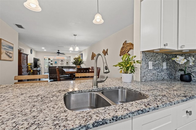 kitchen with white cabinetry, sink, light stone countertops, backsplash, and decorative light fixtures