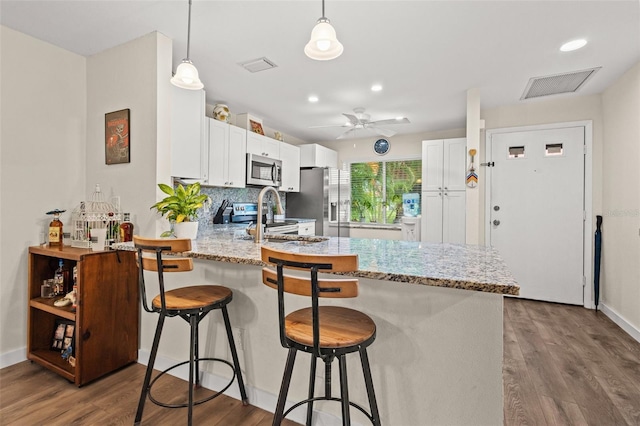 kitchen featuring kitchen peninsula, white cabinets, wood-type flooring, and appliances with stainless steel finishes