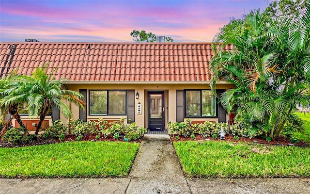 view of front facade featuring a tiled roof, a front lawn, and stucco siding