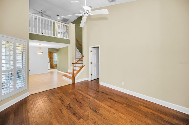 unfurnished living room featuring ceiling fan, a towering ceiling, and light wood-type flooring