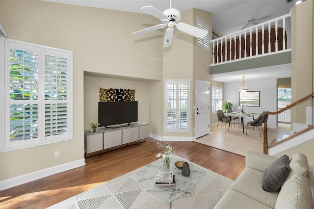 living room with ceiling fan, wood-type flooring, and a towering ceiling