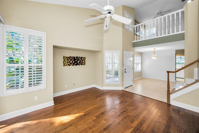 unfurnished living room with wood-type flooring, a towering ceiling, and ceiling fan