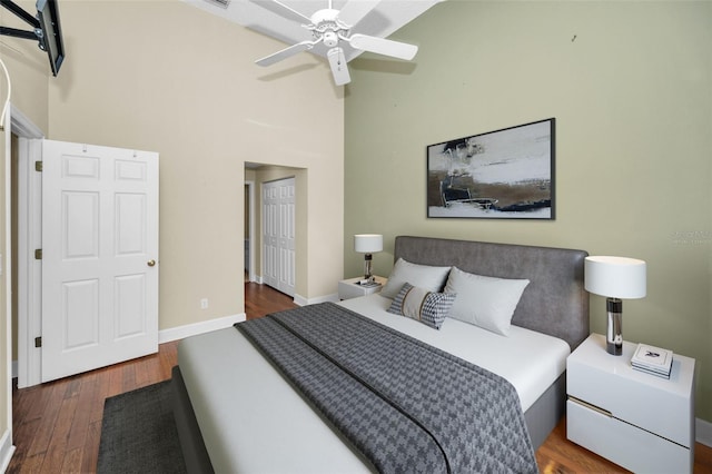 bedroom with ceiling fan, a towering ceiling, and dark hardwood / wood-style floors