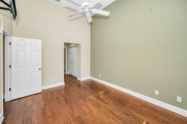 unfurnished bedroom featuring wood-type flooring, a towering ceiling, and ceiling fan