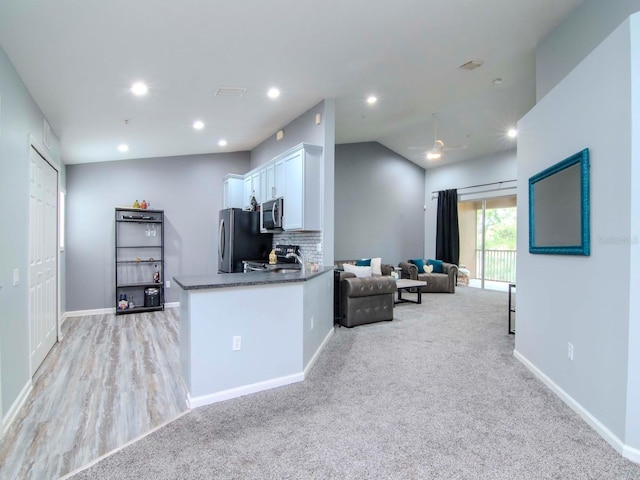 kitchen with light carpet, kitchen peninsula, backsplash, stainless steel appliances, and white cabinets