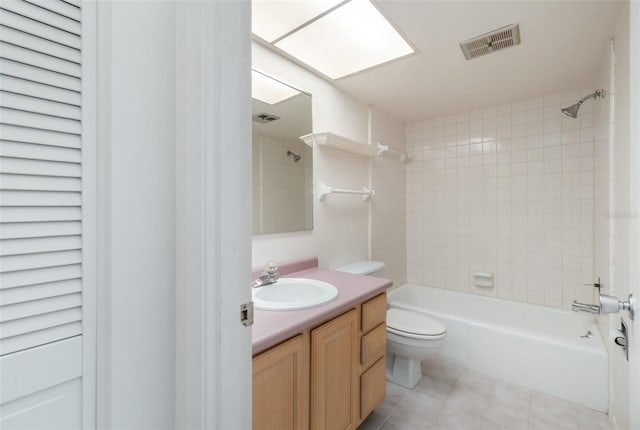 full bathroom featuring vanity, a skylight, tile patterned flooring, tiled shower / bath combo, and toilet