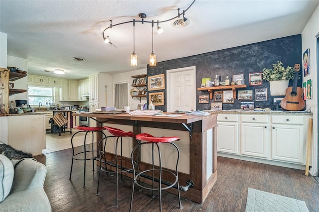 kitchen featuring dark hardwood / wood-style flooring, a textured ceiling, decorative light fixtures, white cabinets, and a center island