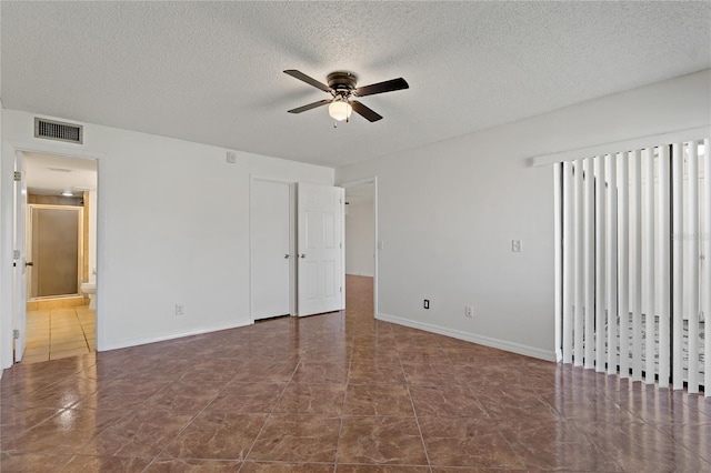 spare room featuring dark tile patterned flooring, ceiling fan, and a textured ceiling