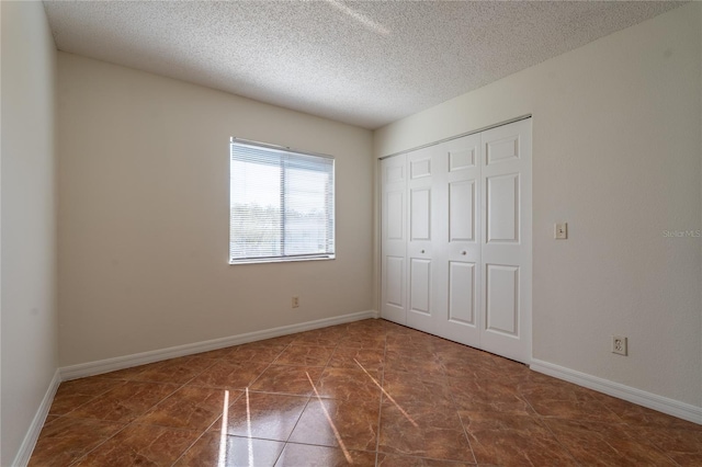 unfurnished bedroom featuring a textured ceiling, dark tile patterned floors, and a closet