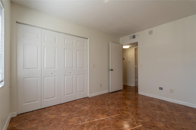 unfurnished bedroom with a textured ceiling, dark tile patterned flooring, and a closet