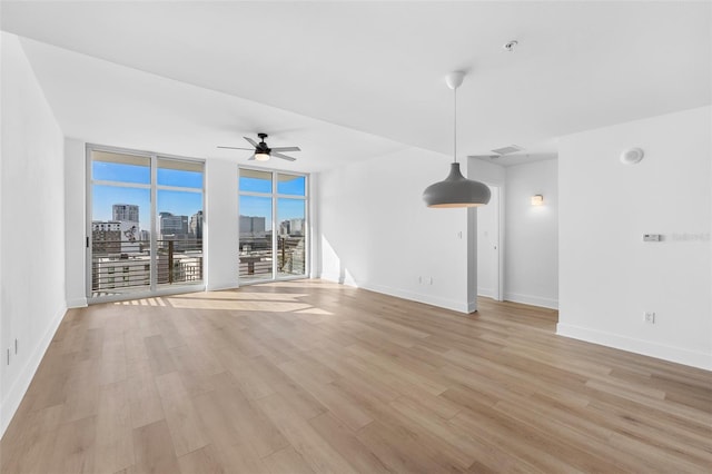 unfurnished living room with a wall of windows, ceiling fan, and light wood-type flooring