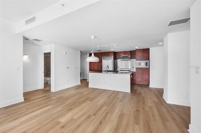 kitchen with decorative backsplash, light wood-type flooring, pendant lighting, built in appliances, and an island with sink