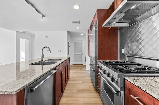 kitchen featuring light wood-type flooring, light stone counters, high end appliances, and wall chimney range hood