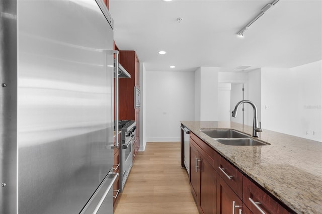 kitchen with light wood-type flooring, stainless steel appliances, light stone counters, and sink