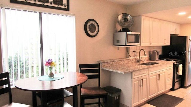 kitchen with white cabinets, range, light stone countertops, and sink