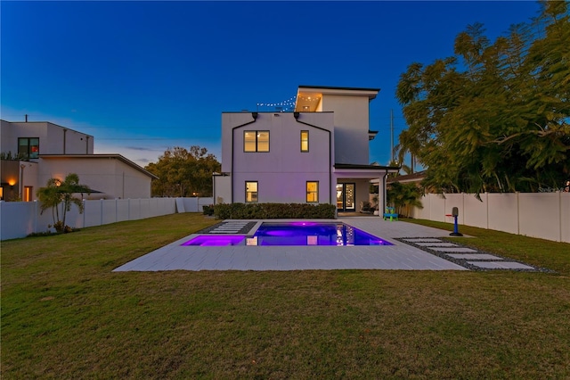 back house at dusk with a patio, a fenced in pool, and a lawn