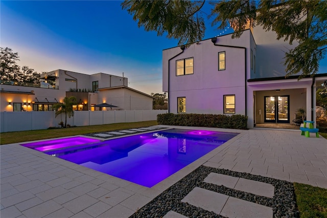 pool at dusk featuring a patio area, an in ground hot tub, and french doors