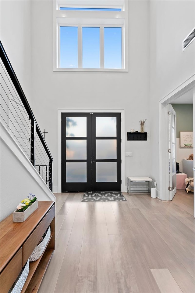 foyer entrance featuring french doors, wood-type flooring, and a high ceiling