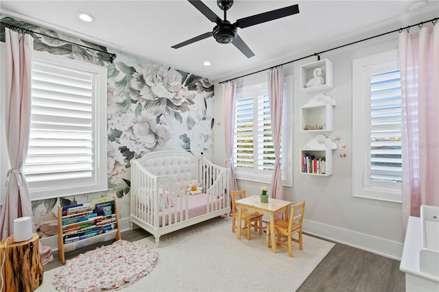 bedroom featuring hardwood / wood-style flooring, ceiling fan, and a nursery area