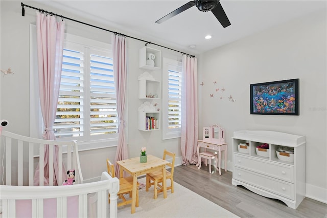 bedroom with a crib, light wood-type flooring, and ceiling fan