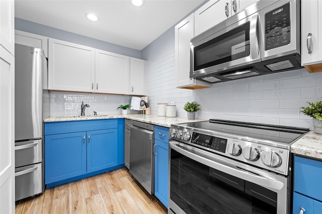 kitchen with blue cabinetry, white cabinetry, stainless steel appliances, light hardwood / wood-style floors, and decorative backsplash