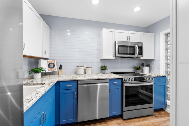 kitchen with blue cabinetry, white cabinets, stainless steel appliances, and light hardwood / wood-style floors