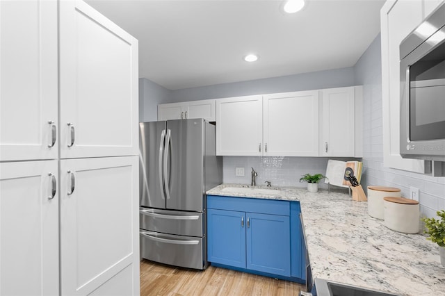 kitchen featuring light wood-type flooring, stainless steel appliances, sink, blue cabinetry, and white cabinets