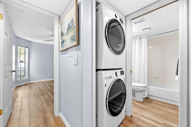 laundry area featuring a textured ceiling, stacked washer / dryer, and light hardwood / wood-style flooring