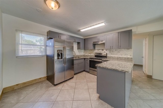 kitchen featuring light stone countertops, backsplash, a textured ceiling, stainless steel appliances, and gray cabinets