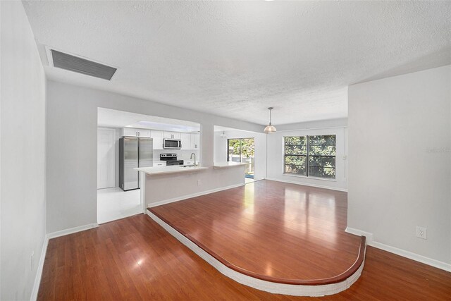 unfurnished dining area featuring sink, light hardwood / wood-style floors, and a textured ceiling