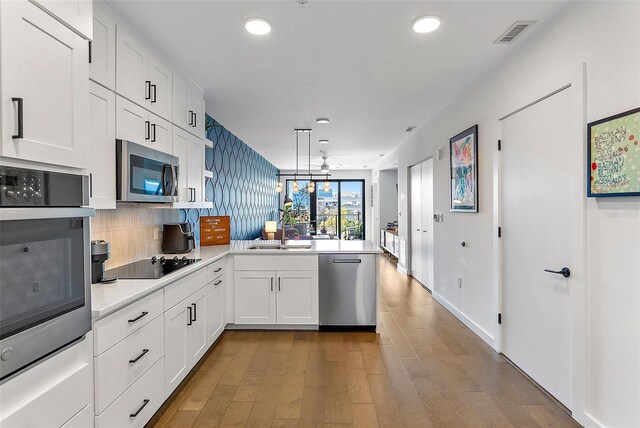 kitchen with kitchen peninsula, appliances with stainless steel finishes, decorative backsplash, pendant lighting, and white cabinets