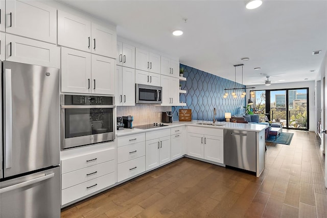 kitchen with kitchen peninsula, appliances with stainless steel finishes, pendant lighting, white cabinets, and sink