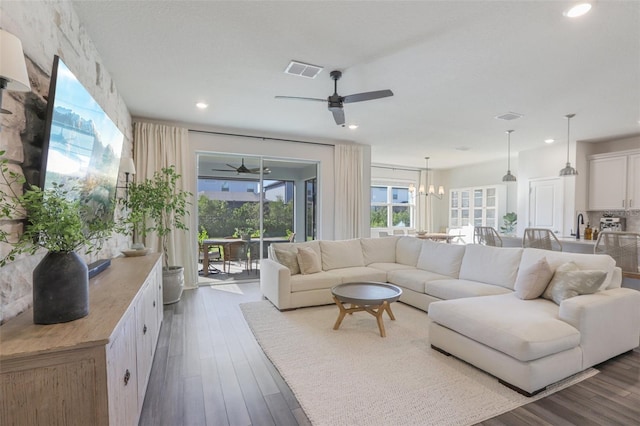 living room with ceiling fan with notable chandelier, dark hardwood / wood-style flooring, and sink