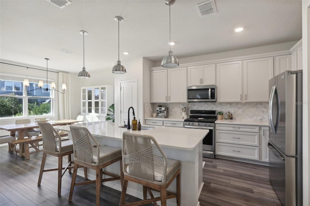 kitchen featuring stainless steel appliances, sink, pendant lighting, white cabinets, and an island with sink