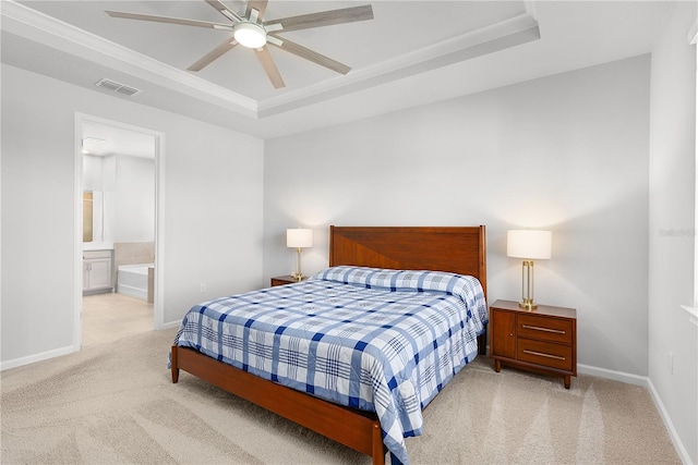 bedroom with a tray ceiling, ensuite bathroom, ceiling fan, and light colored carpet