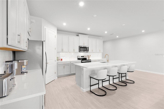 kitchen featuring a kitchen breakfast bar, sink, light wood-type flooring, appliances with stainless steel finishes, and white cabinetry