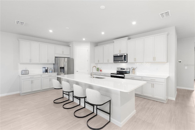 kitchen with white cabinetry, sink, stainless steel appliances, and a center island with sink