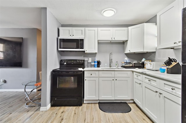 kitchen featuring light stone countertops, white cabinetry, sink, black electric range, and light wood-type flooring