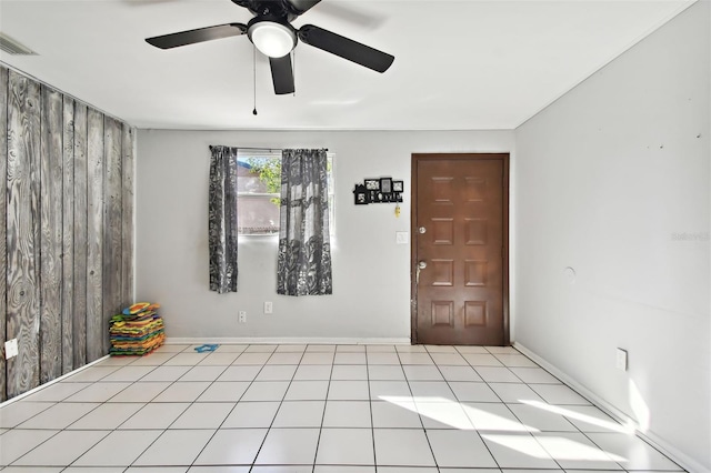 unfurnished room with light tile patterned flooring, ceiling fan, and wood walls