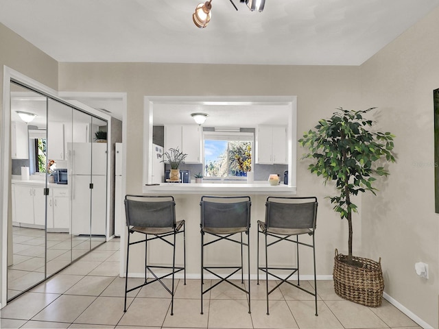 kitchen with white cabinets, a breakfast bar, light tile patterned floors, and a wealth of natural light