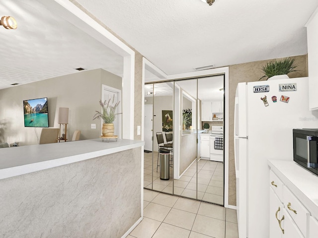 kitchen with white appliances, white cabinetry, a textured ceiling, and light tile patterned floors