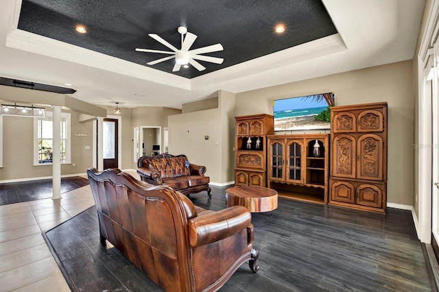 living room featuring a raised ceiling, ceiling fan, ornamental molding, dark hardwood / wood-style flooring, and decorative columns