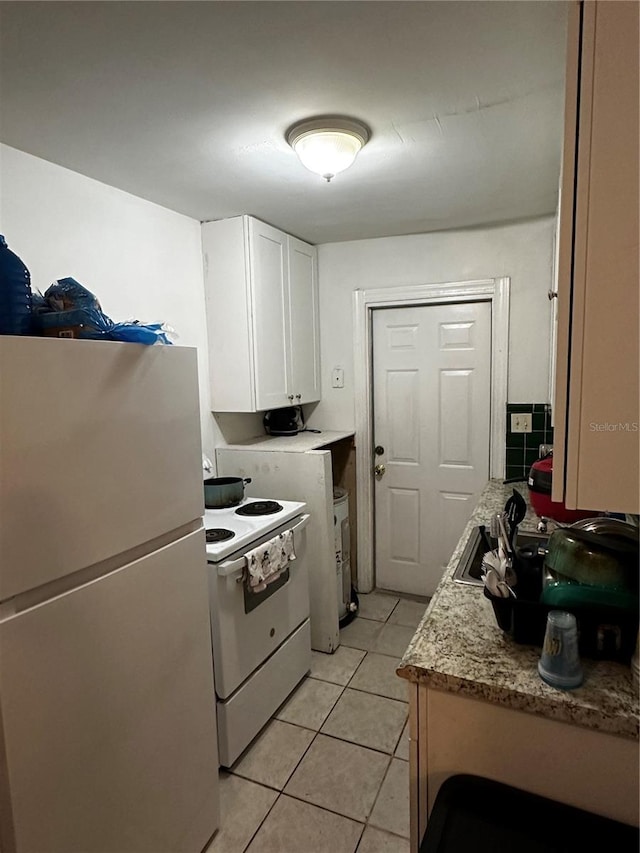 kitchen featuring light stone counters, white appliances, sink, light tile patterned floors, and white cabinetry