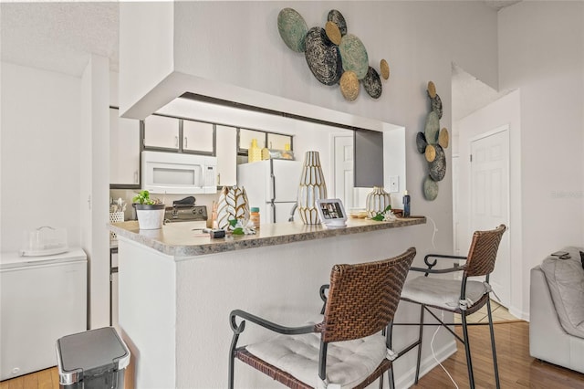 kitchen with white appliances, white cabinets, hardwood / wood-style flooring, a textured ceiling, and kitchen peninsula